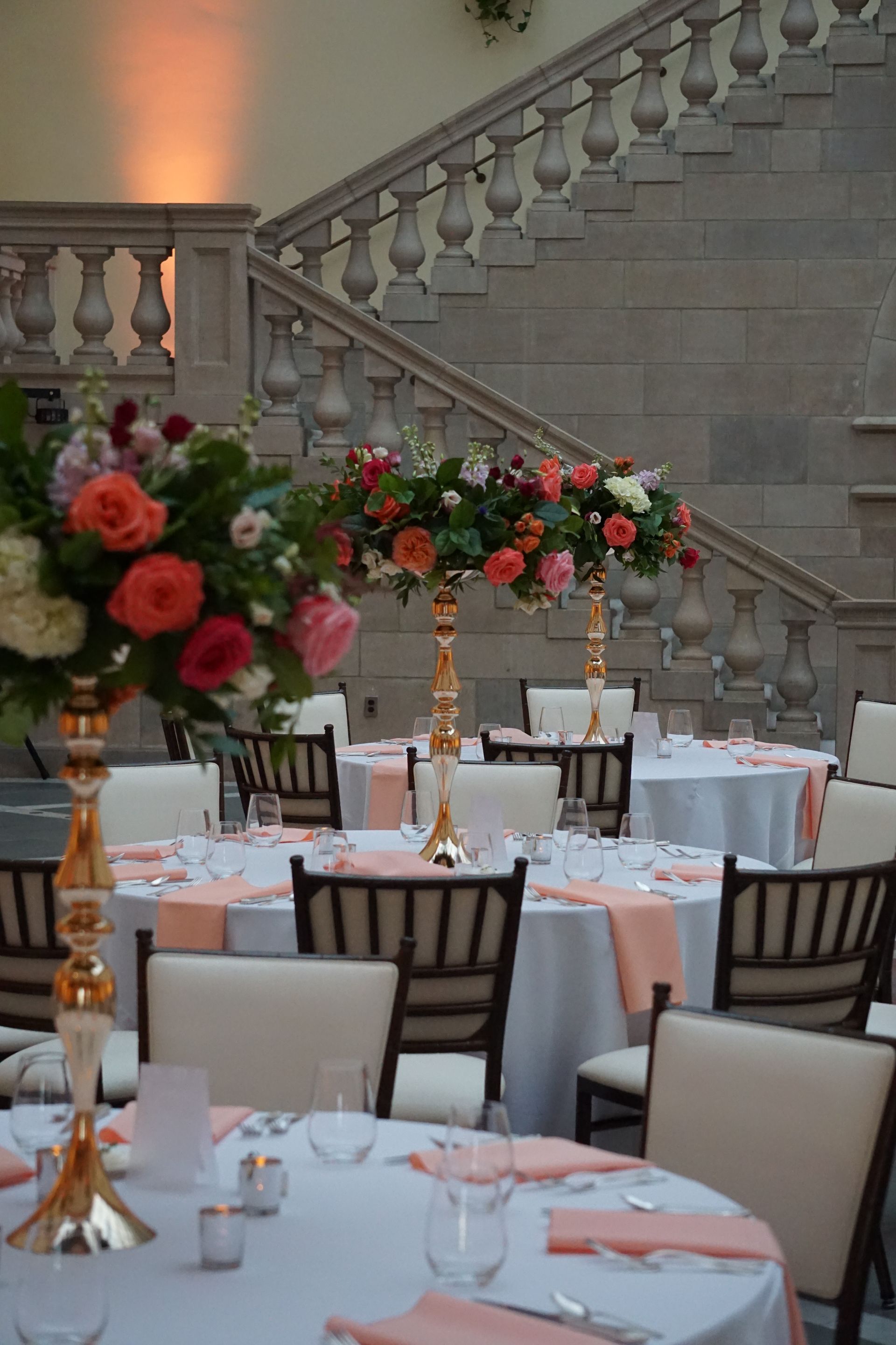 A room with tables and chairs set up for a wedding reception with stairs in the background.