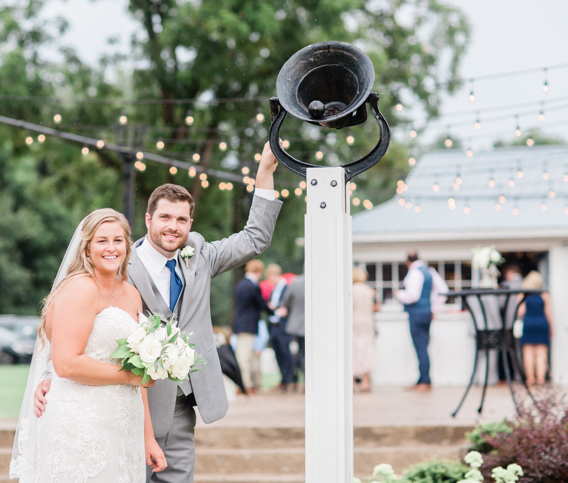 A bride and groom are posing for a picture in front of a bell.