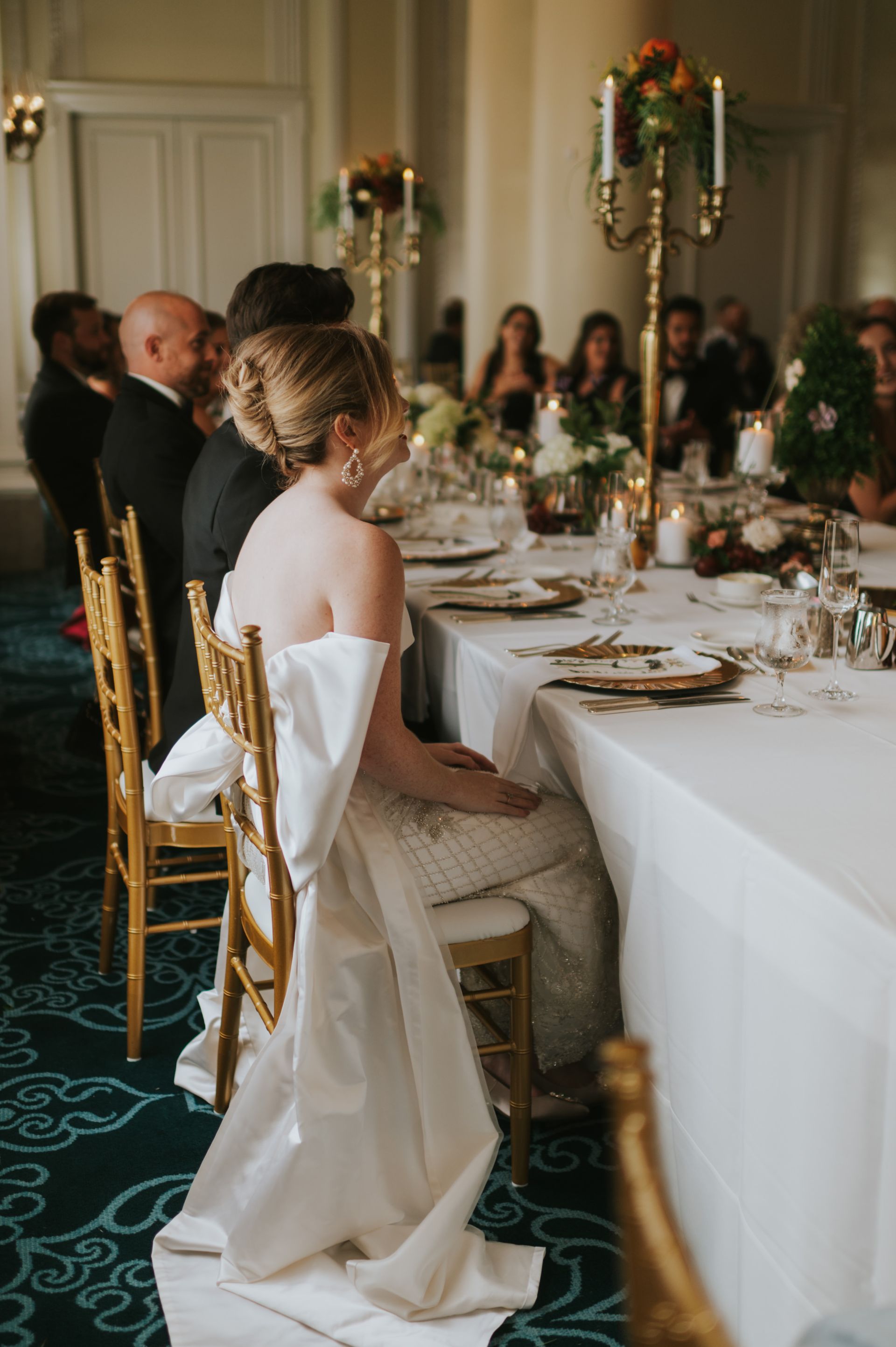 A bride and groom are sitting at a long table at a wedding reception.