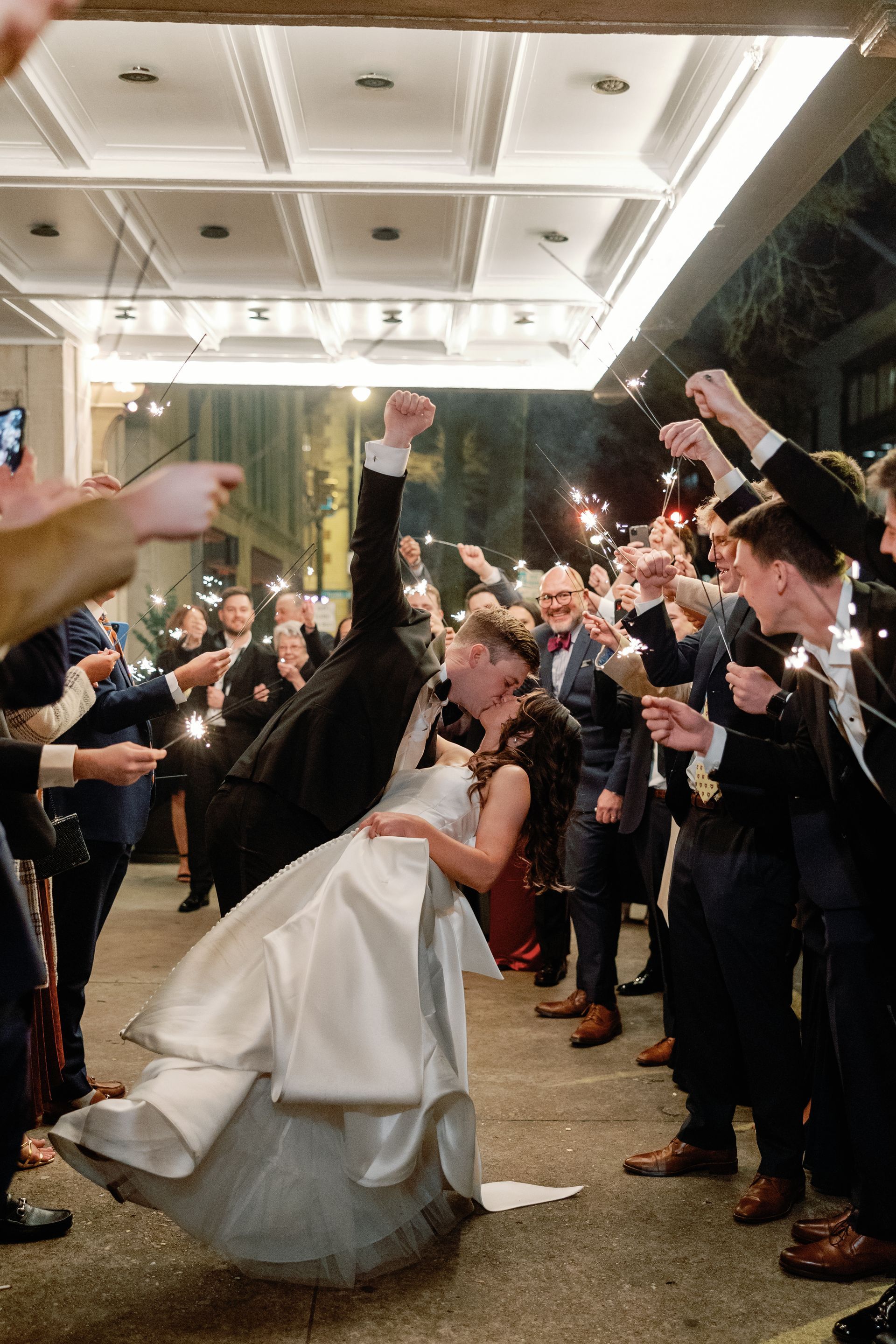A bride and groom are kissing in front of a crowd of people holding sparklers.