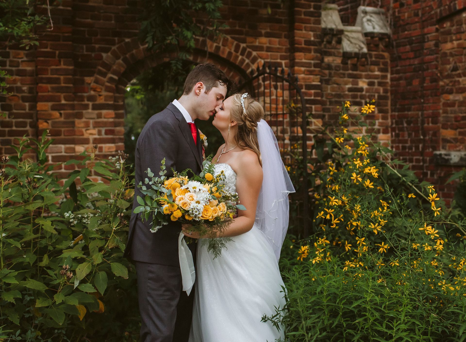 A bride and groom are kissing in front of a brick wall.