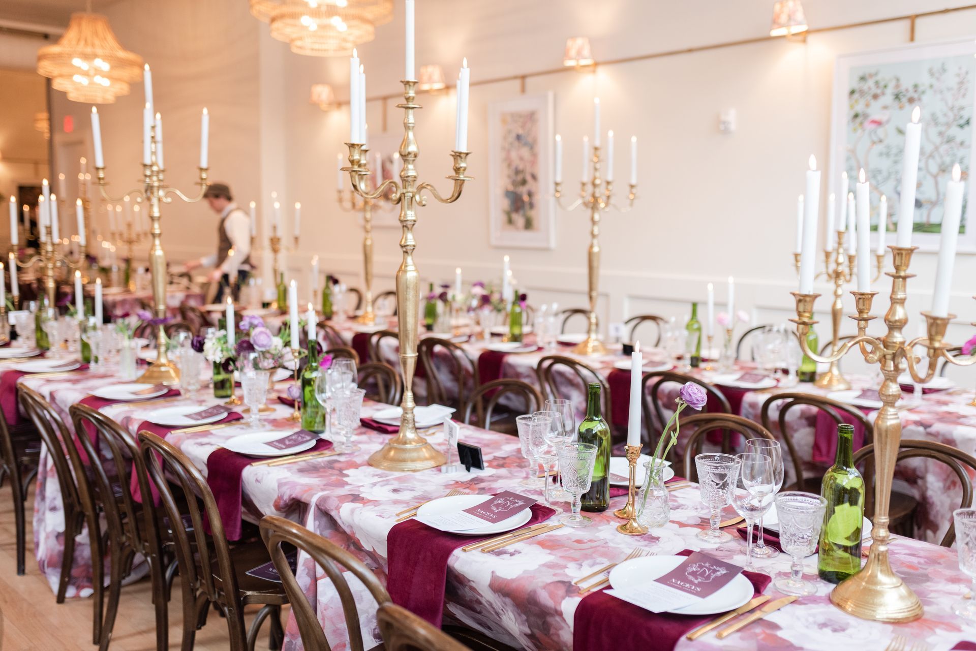 A long table with plates , candles , and chairs set for a wedding reception.