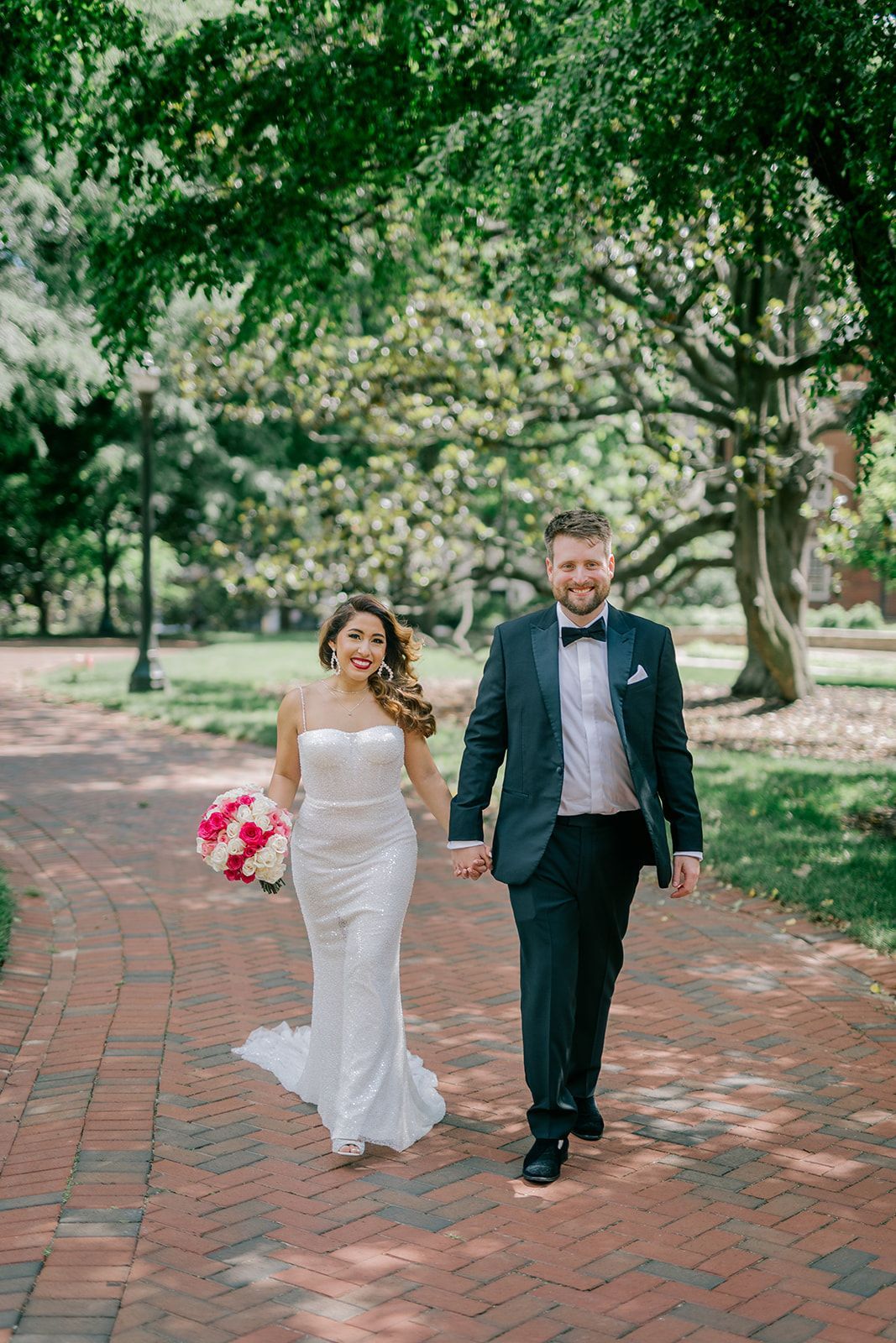 A bride and groom are walking down a brick path holding hands.