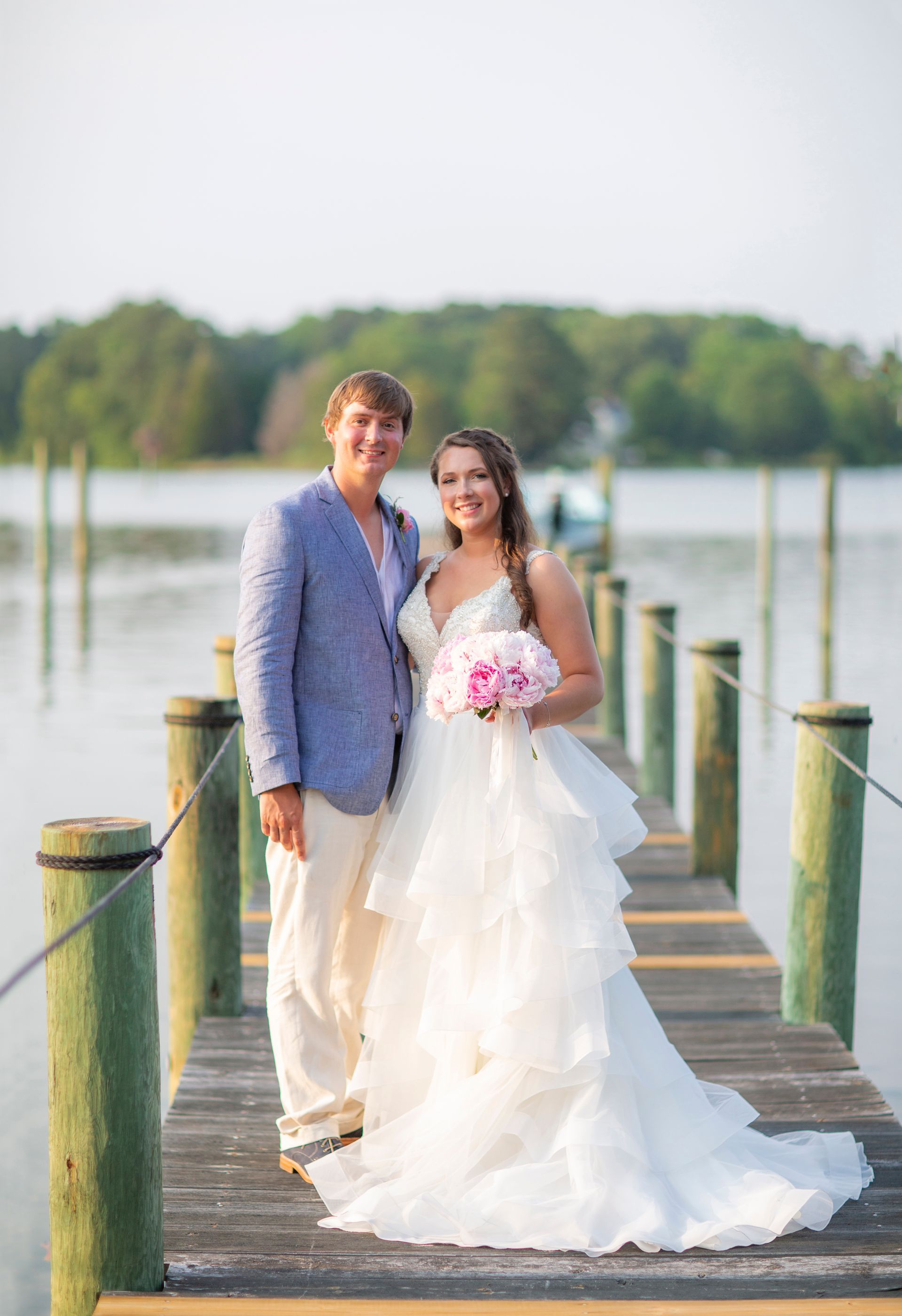 A bride and groom are posing for a picture on a dock.