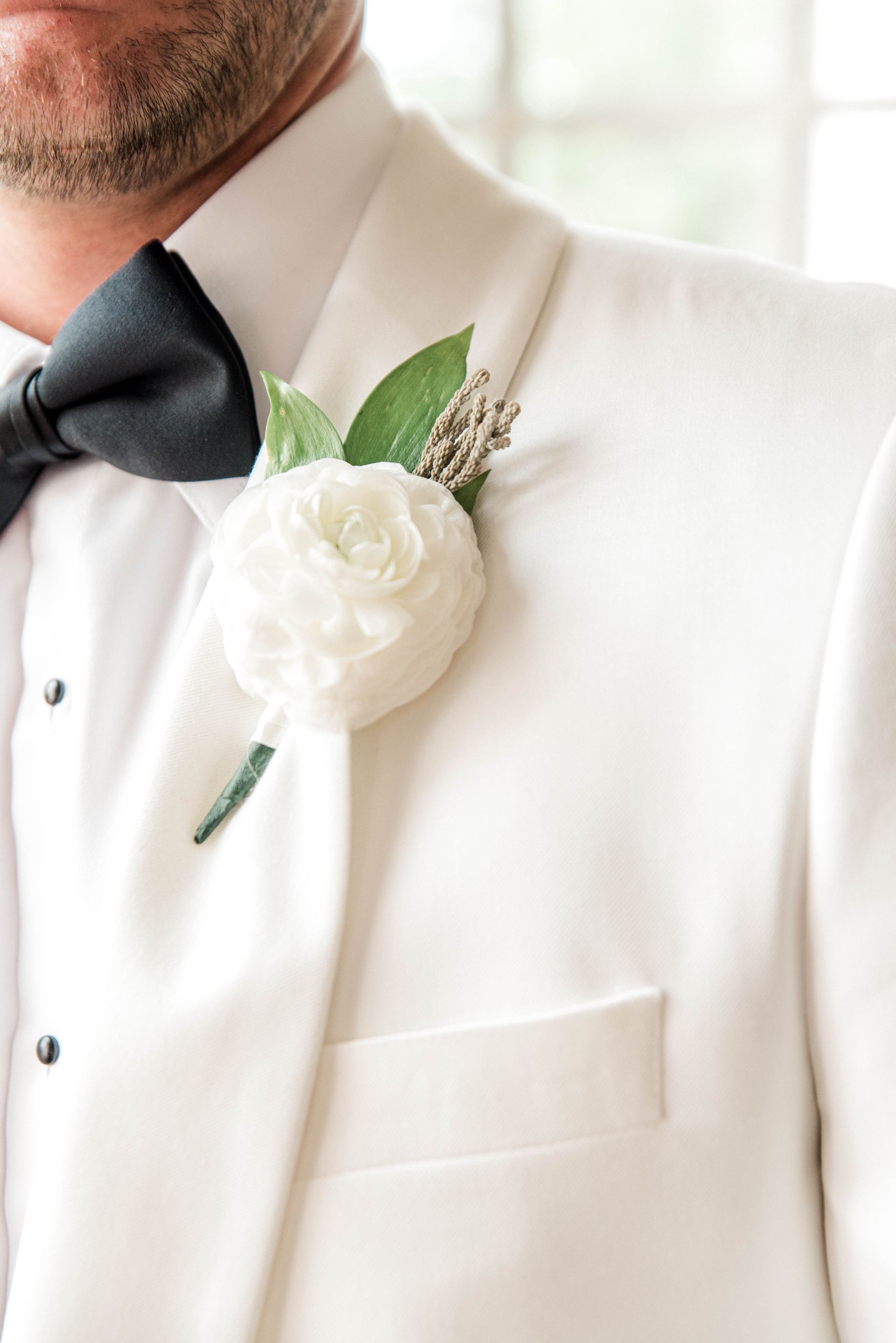 The groom is wearing a white tuxedo and a black bow tie.