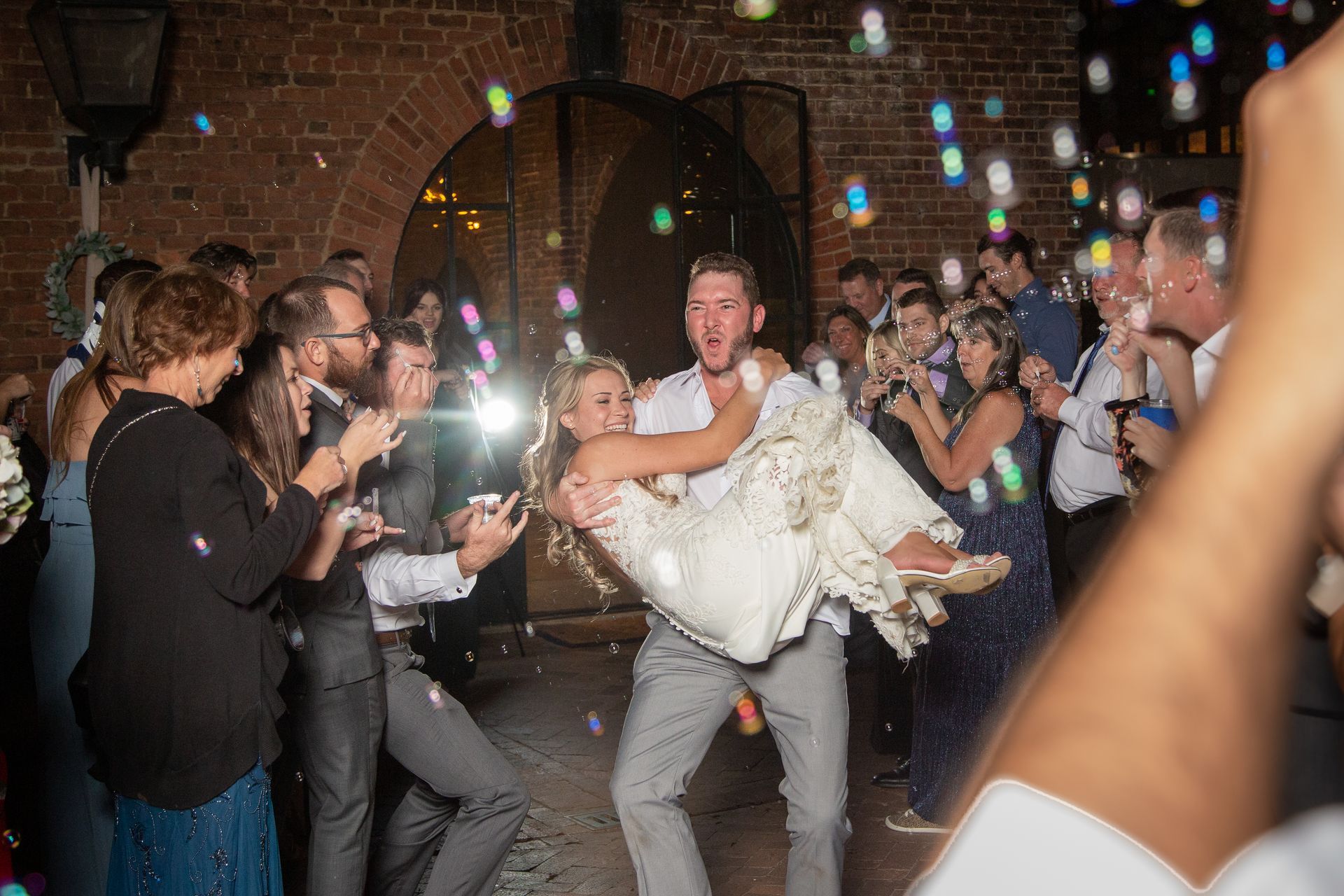 A man is carrying a woman in his arms at a wedding reception.