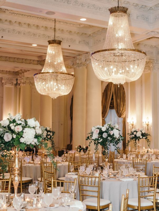 A large room with tables and chairs set up for a wedding reception with chandeliers hanging from the ceiling.