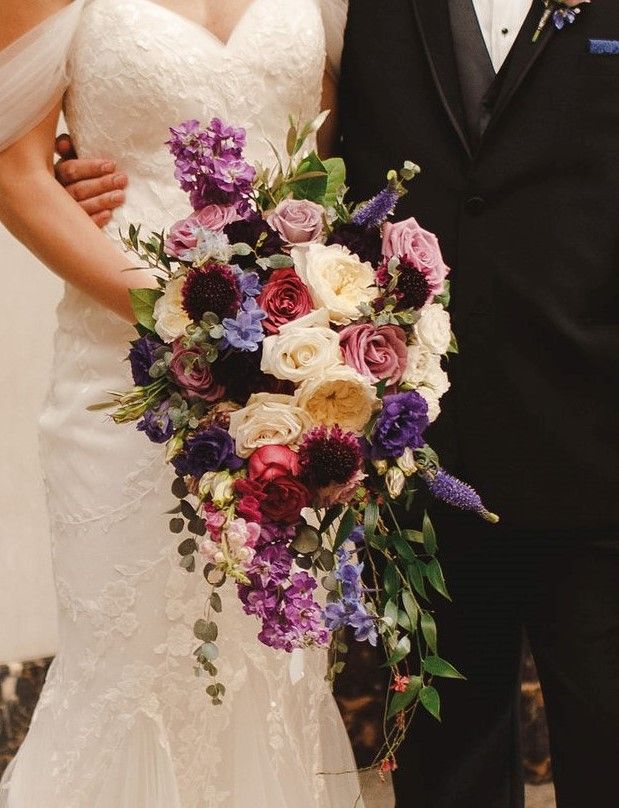 A bride and groom holding a bouquet of purple and white flowers