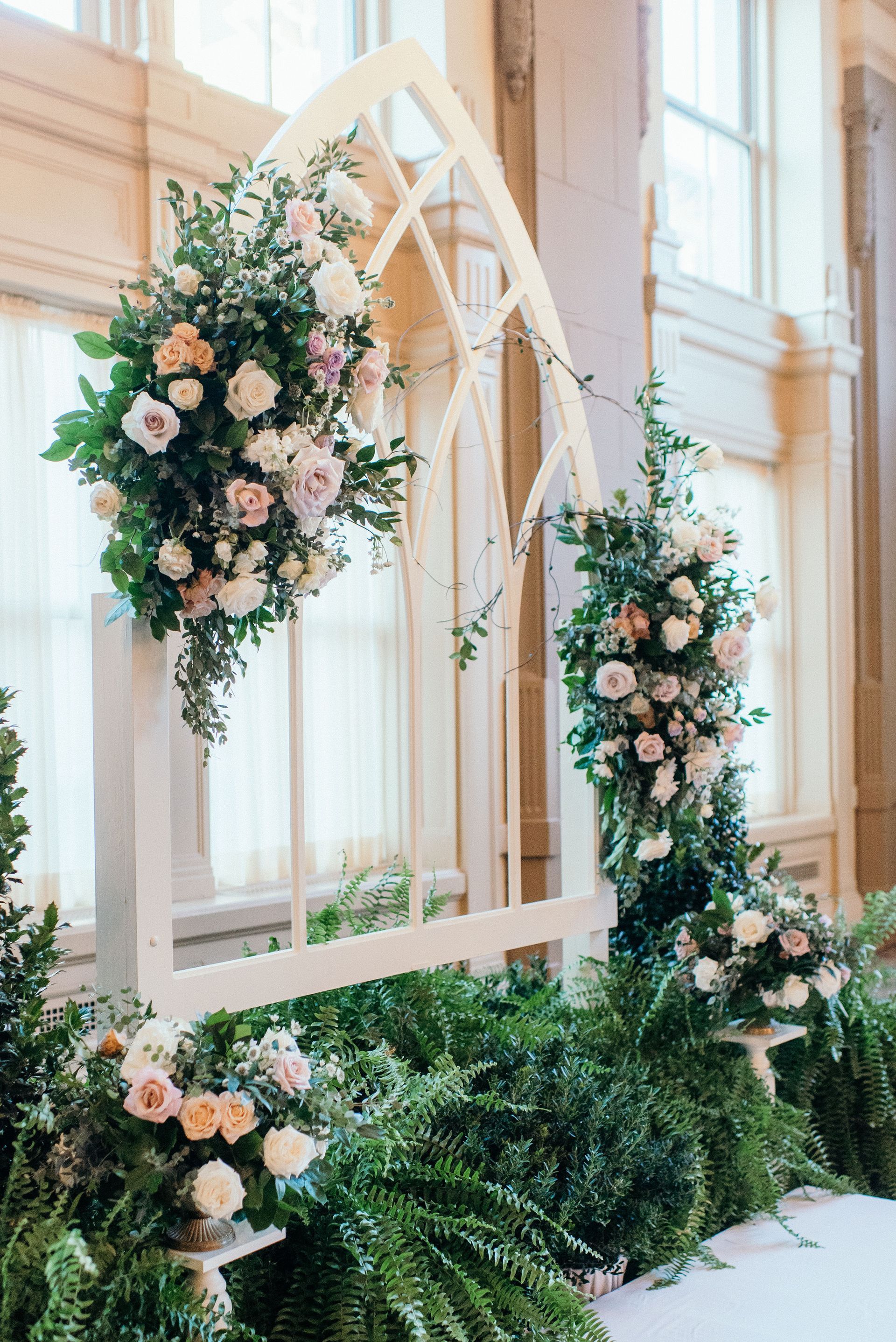 A wooden arch decorated with flowers and ferns for a wedding ceremony.