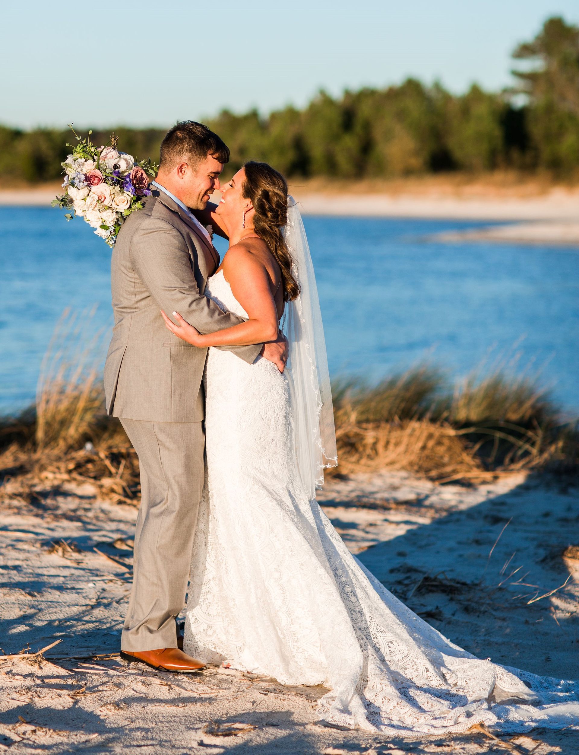 A bride and groom are kissing on the beach.