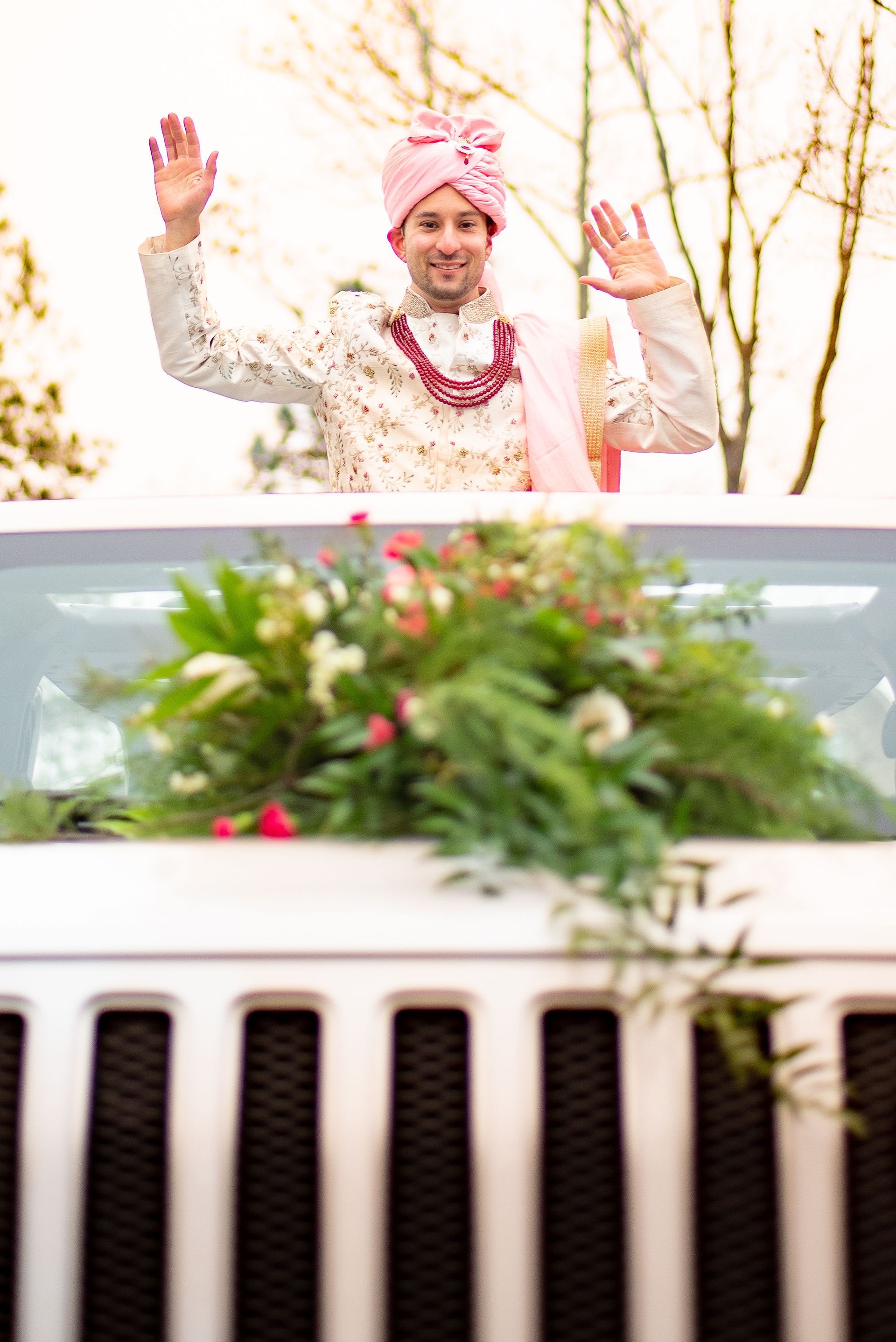A bride and groom are riding in a white jeep decorated with flowers.