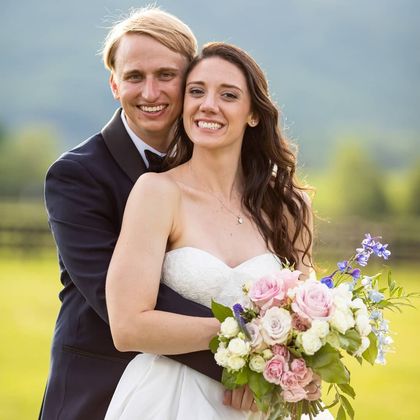 A bride and groom are posing for a picture while the bride is holding a bouquet of flowers.