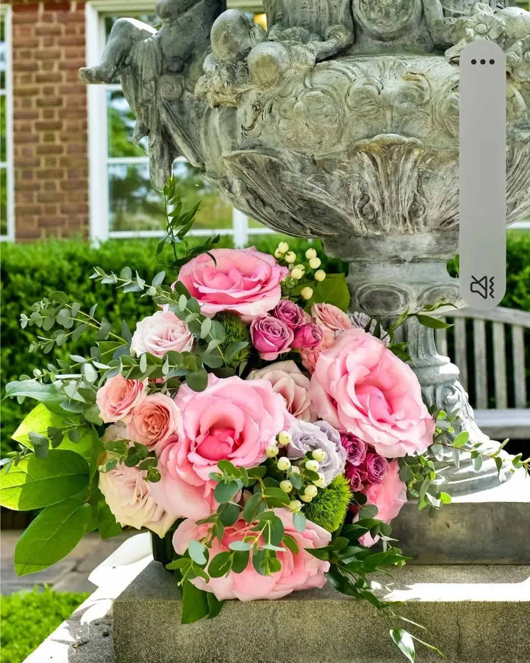 A vase filled with pink roses is sitting on a stone pedestal.