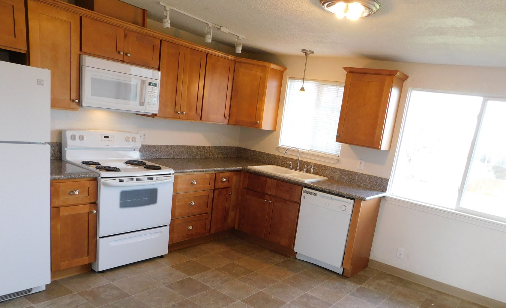 Kitchen with wooden cabinets, white appliances, and a window.