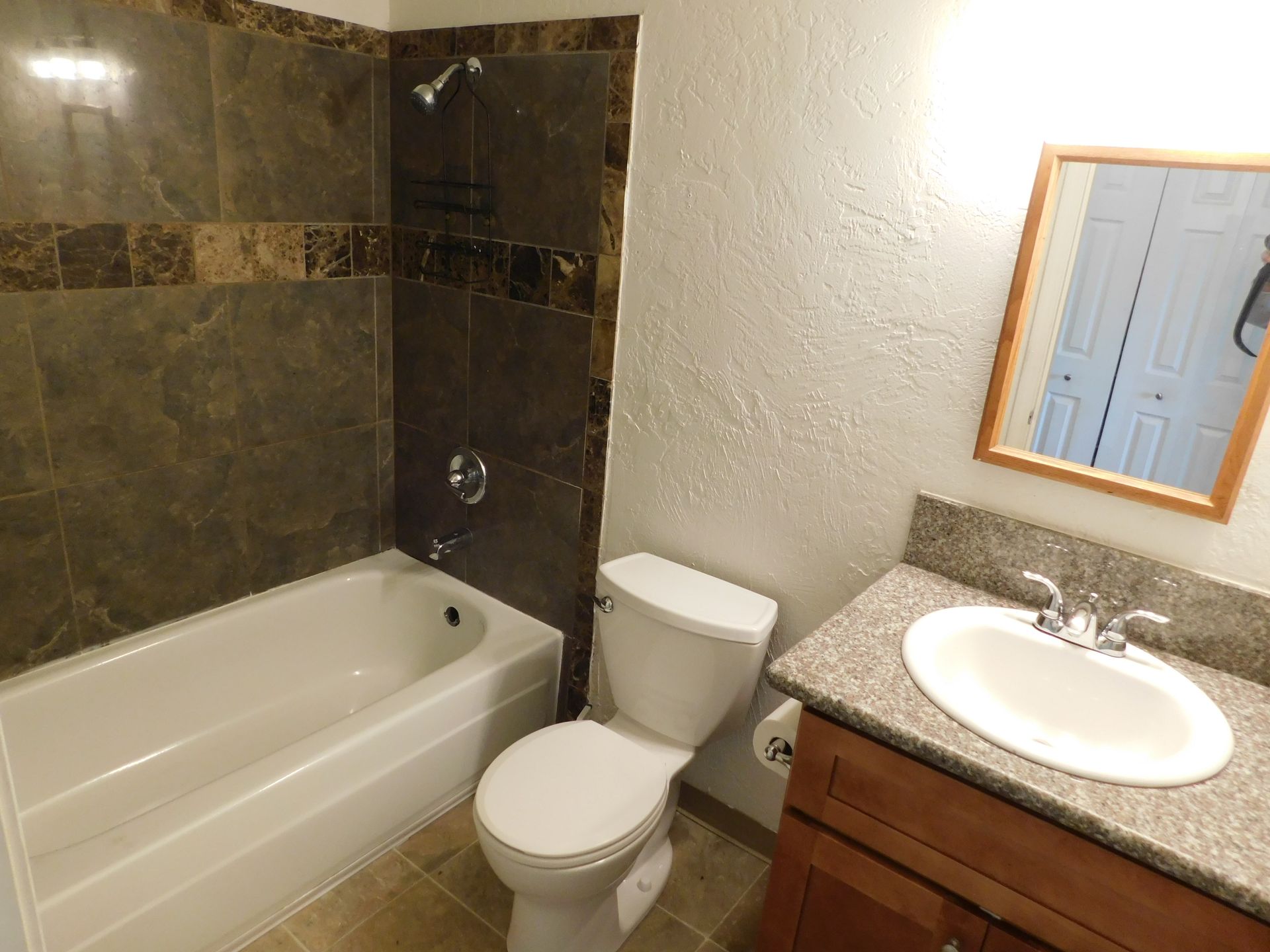 Bathroom with a bathtub, toilet, sink, and mirror. Brown and beige tile.