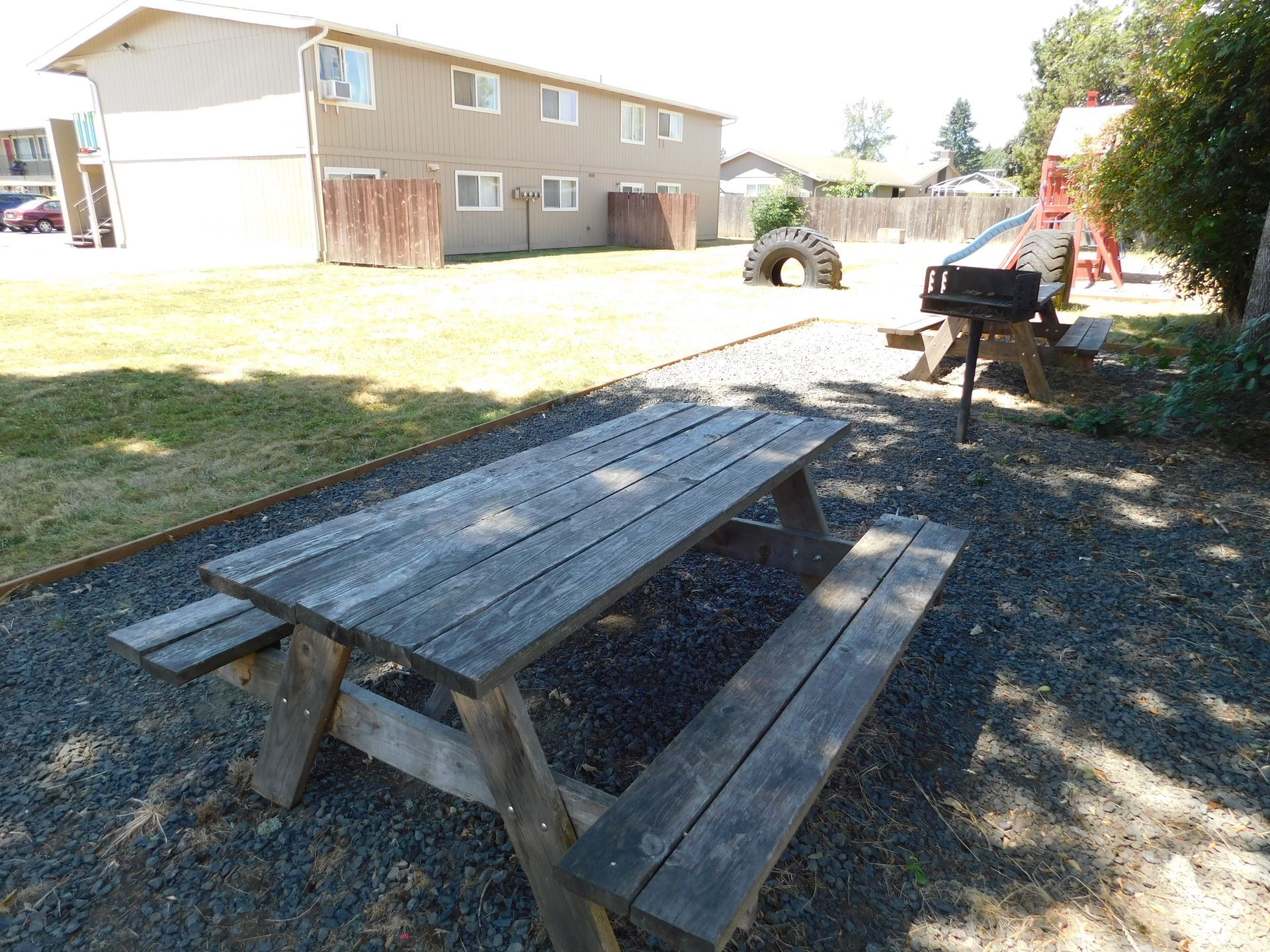 Picnic table and grill in a grassy area outside an apartment building on a sunny day.