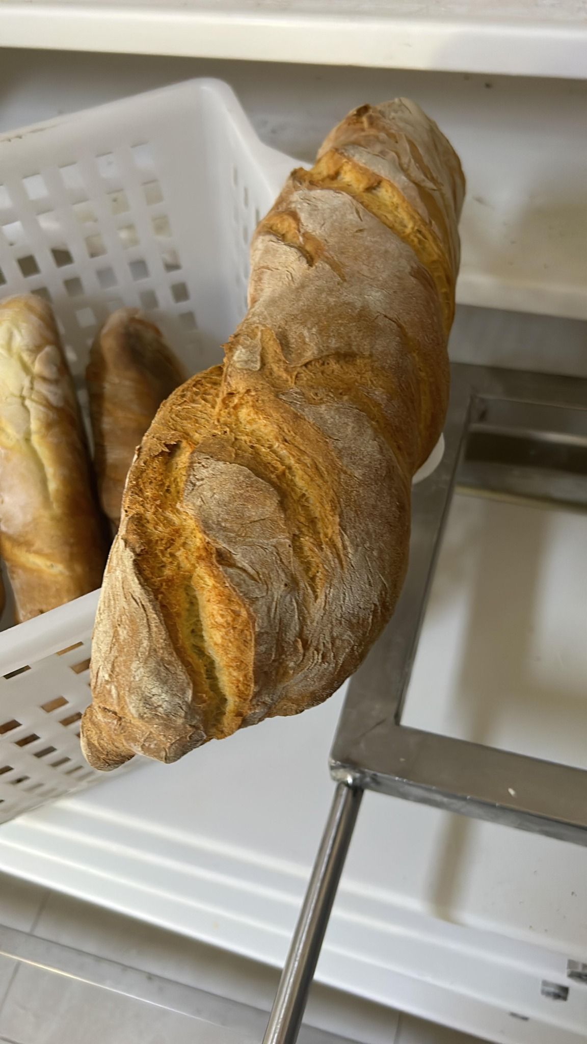 Primo piano di una pagnotta di pane croccante e dorato su una griglia di metallo, con altro pane in un cestino.