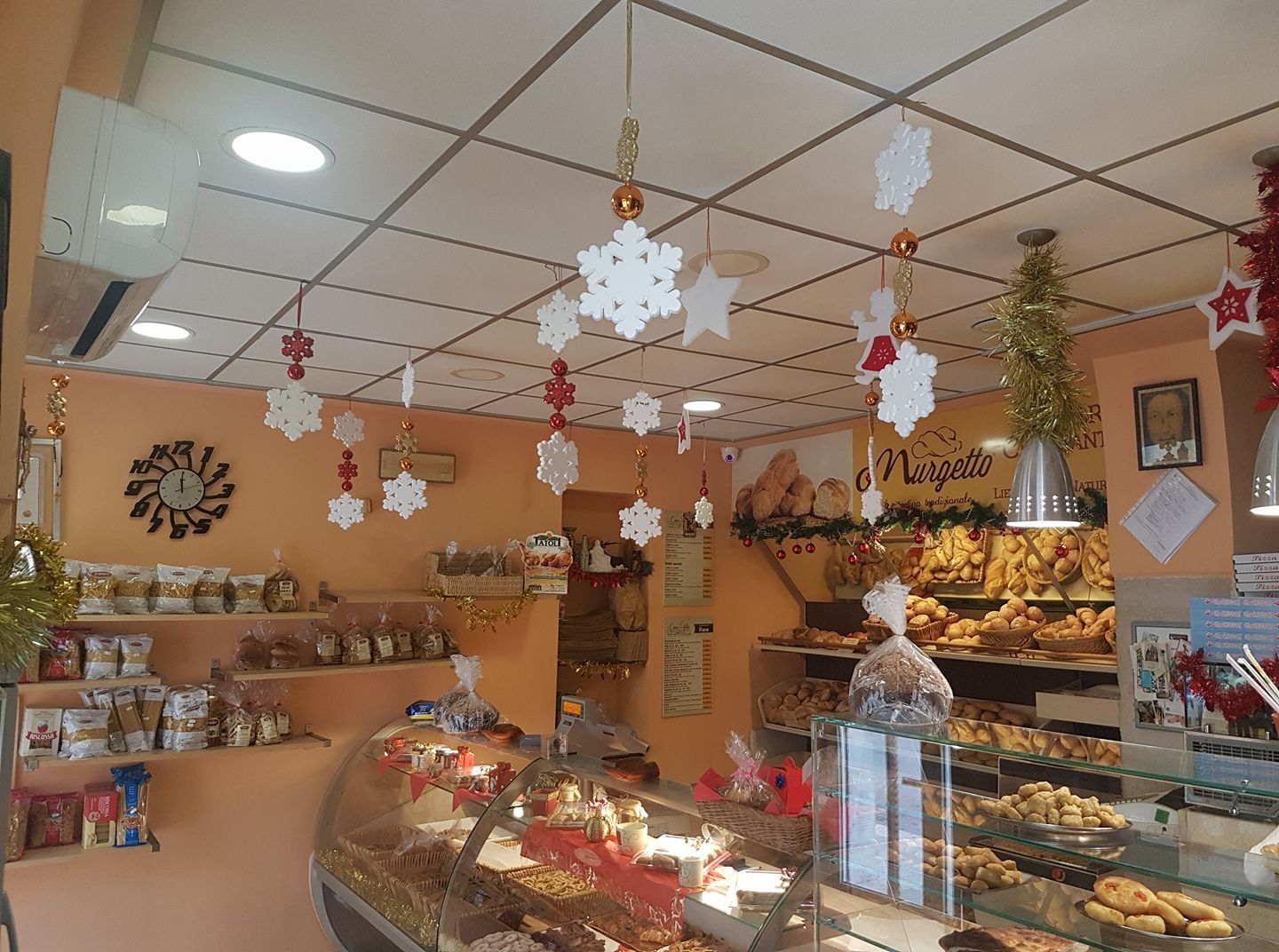 Interno di una panetteria con decorazioni festive, tra cui fiocchi di neve appesi. Le vetrine espongono le prelibatezze.