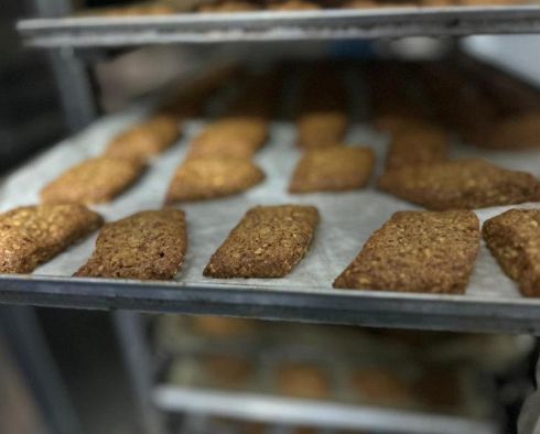 Biscotti di farina d'avena su carta da forno, disposti su ripiani metallici in una cucina commerciale.