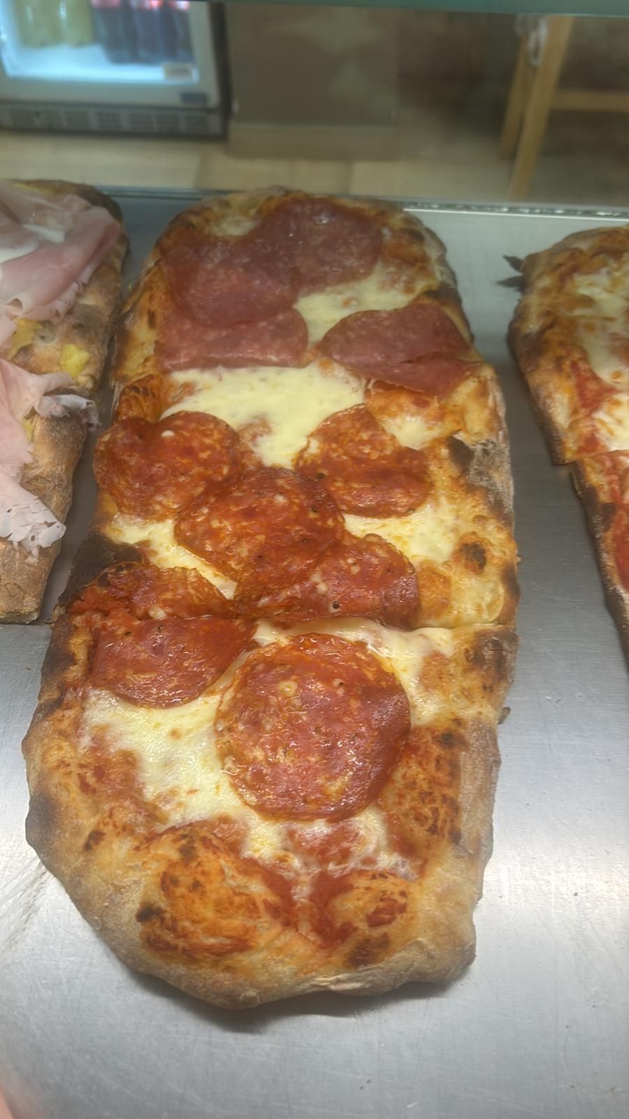 Pizza rettangolare al pepperoni su una superficie metallica, con formaggio e crosta visibili.