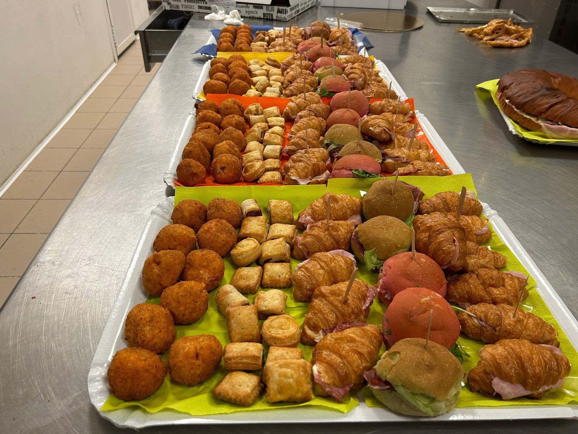Un vassoio di pasticcini assortiti, panini e antipasti su un bancone in acciaio inossidabile.