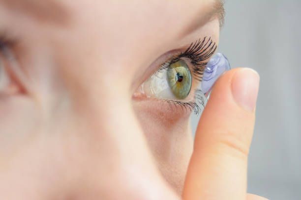 Person inserts a contact lens into a green eye, close-up view.