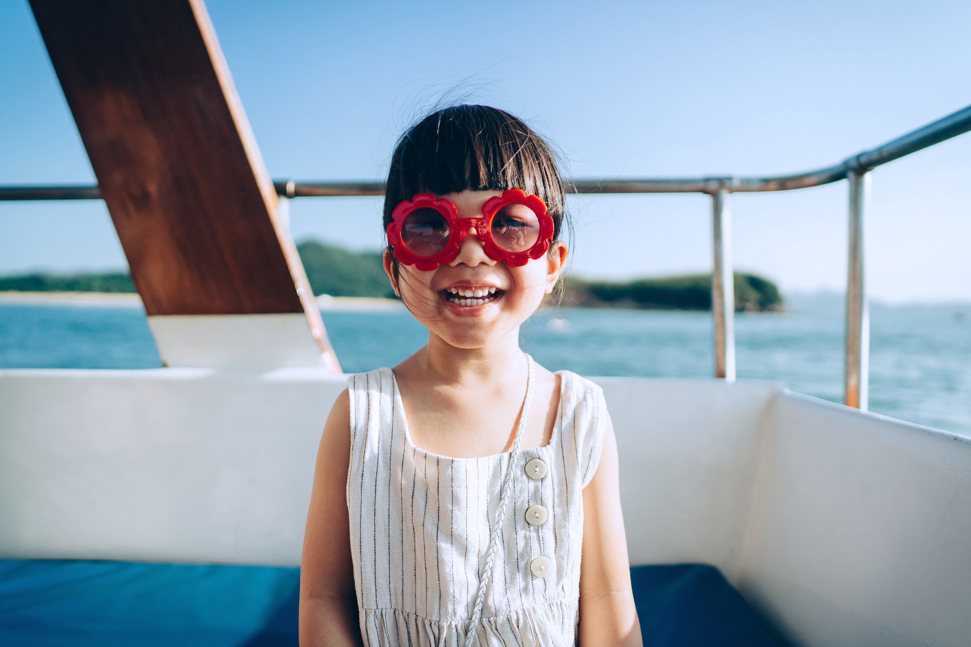 A little girl wearing red sunglasses is sitting on a boat.