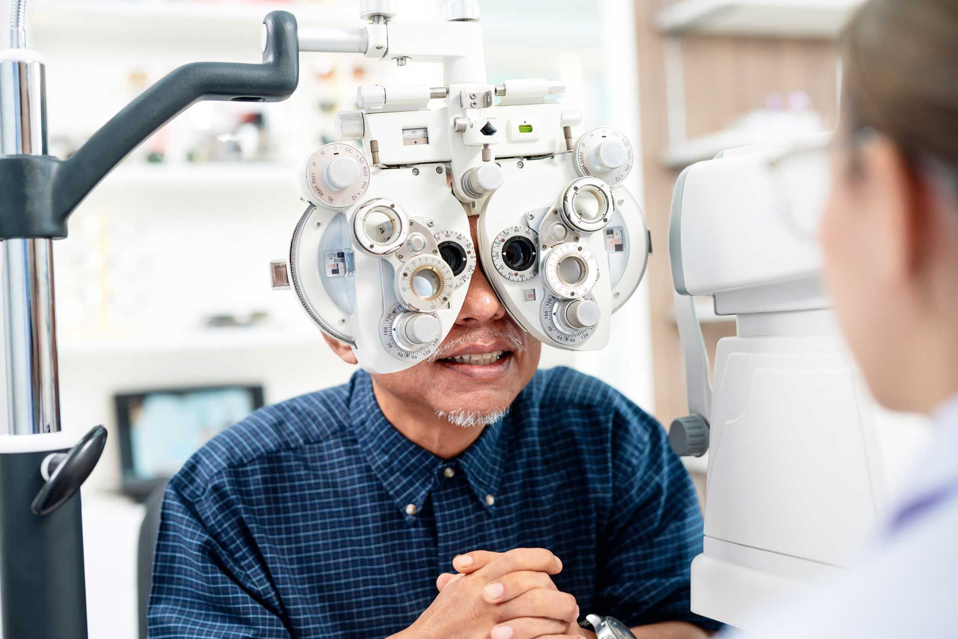 Man having eye exam using a phoropter at an optometry clinic, being examined by a medical professional.