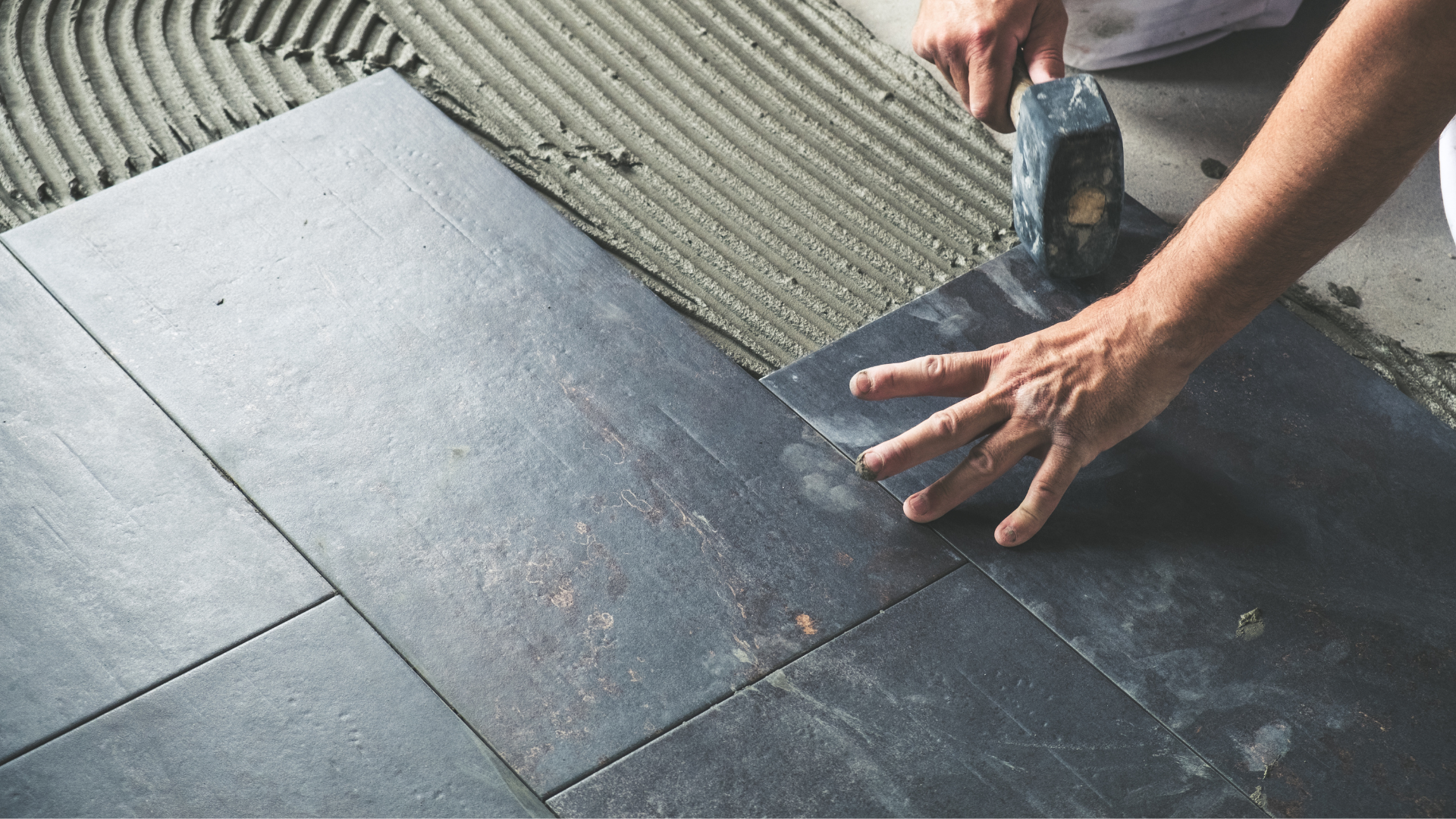A person is laying tiles on the floor with a trowel.