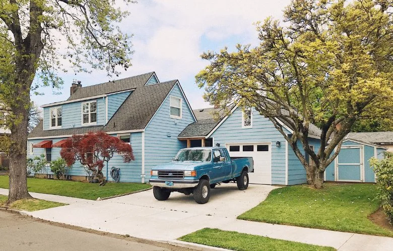 Person on ladder painting blue house exterior.