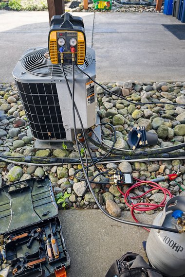 Outdoor equipment setup with solar panel, battery charger, cables, and tools on a rock bed near a walkway