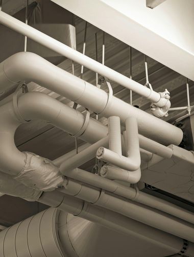 White insulated pipes and ductwork on a ceiling in an industrial utility space