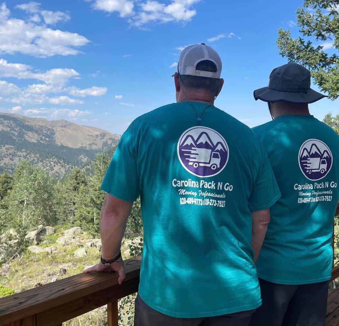 Two men in teal shirts with logo, overlooking a mountain vista from a deck.