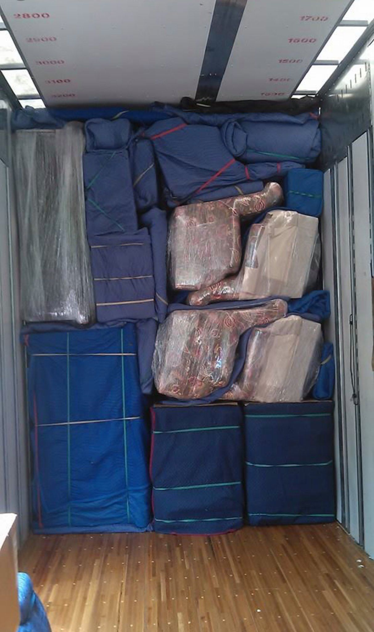 Inside a packed moving truck: furniture, wrapped items, and blue pads.