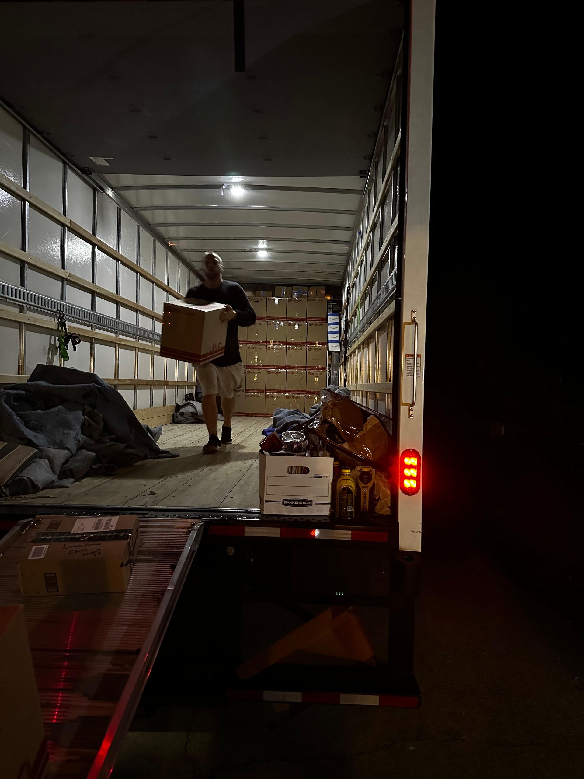Man carrying a box inside a dimly lit truck, loading goods for transport.
