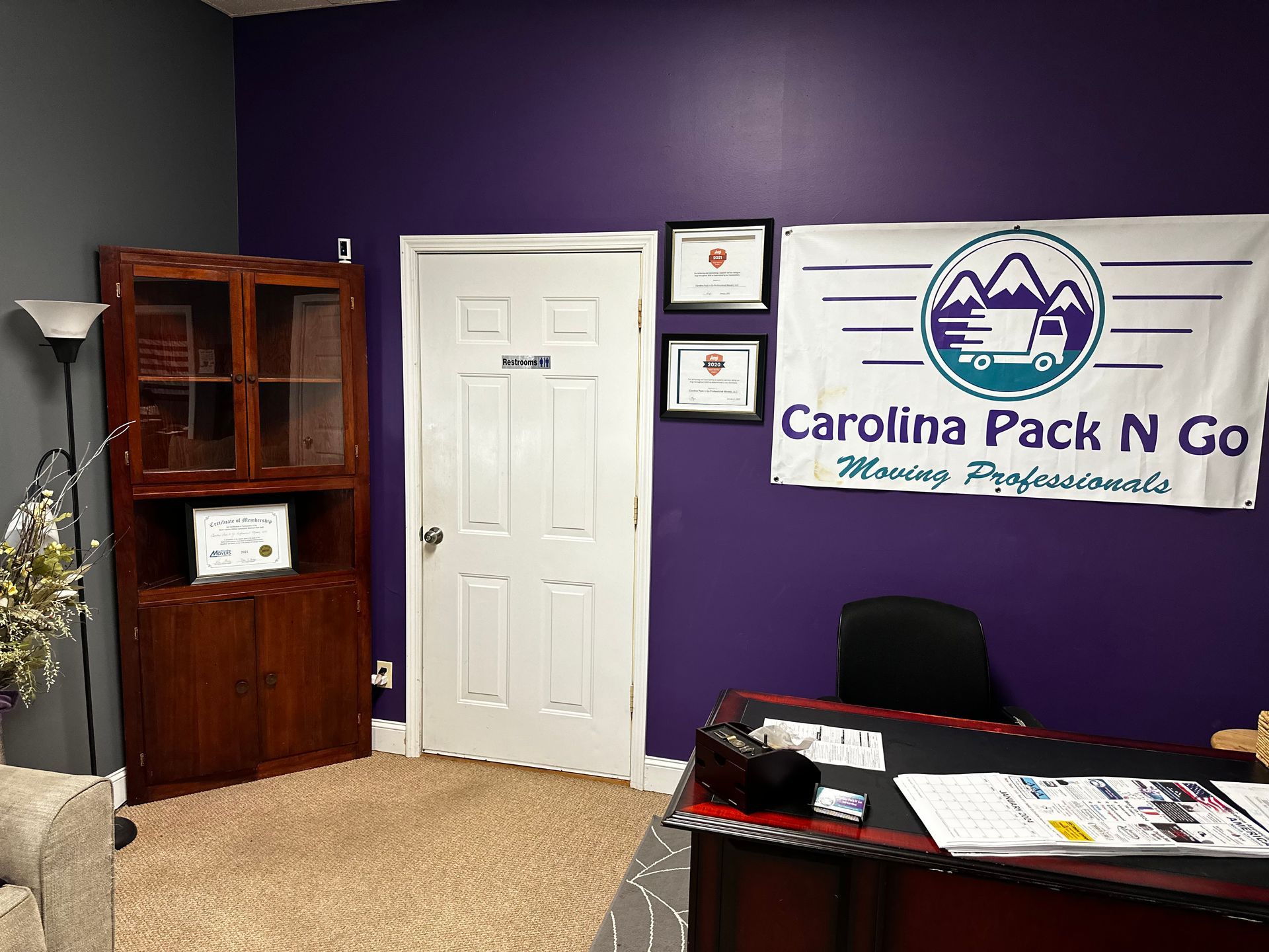 Office interior with Carolina Pack N Go sign, desk, wooden cabinet, and purple wall.