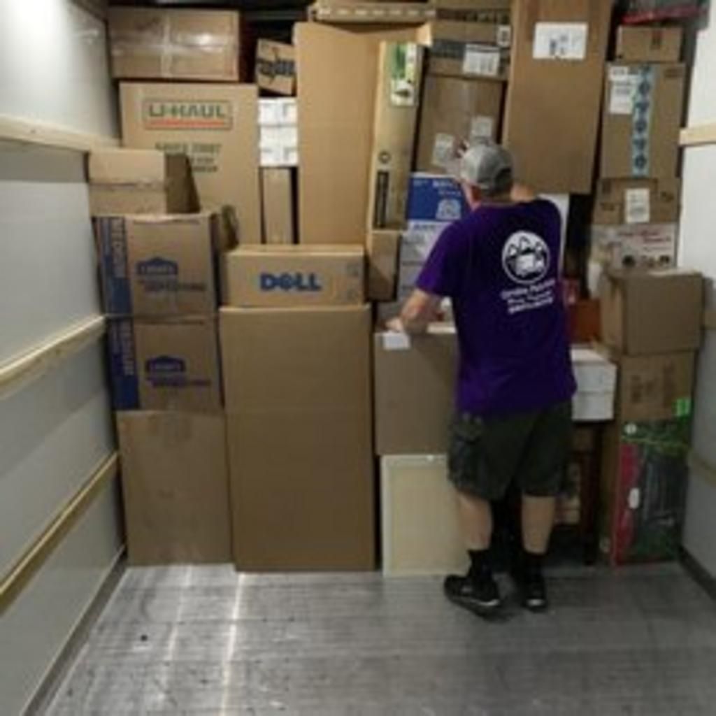 Man in purple shirt packing boxes inside a truck. Truck interior with many cardboard boxes.