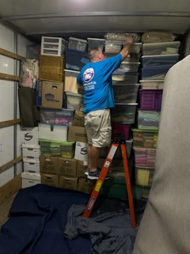 Man on ladder in moving truck stacking boxes.