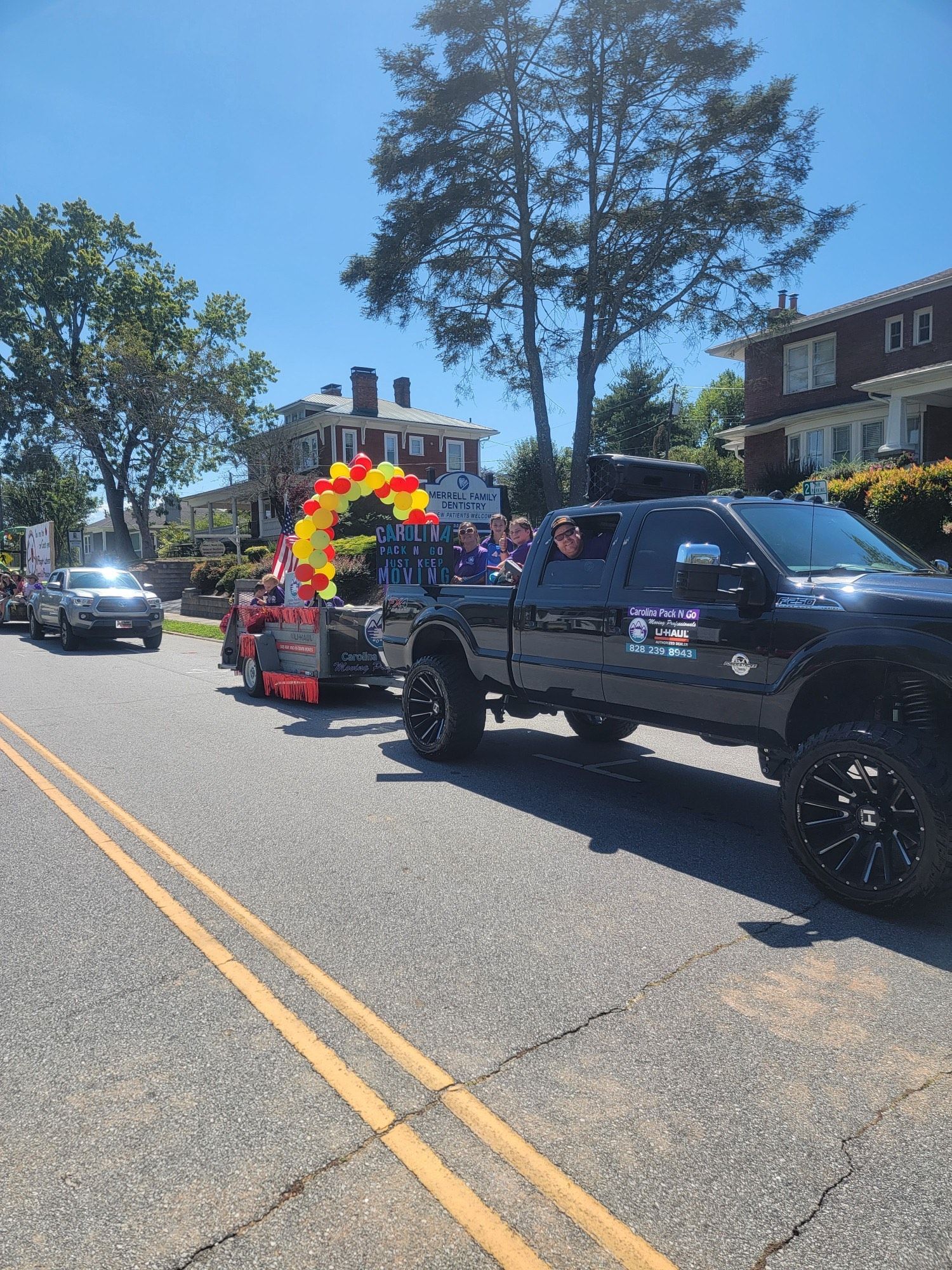 A black truck towing a trailer with balloons, driving down a street in a parade.
