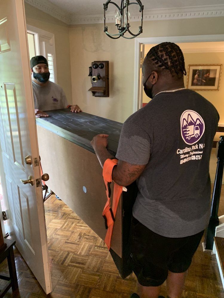 Two movers wearing masks carrying a large, dark-colored object through a doorway into a home.