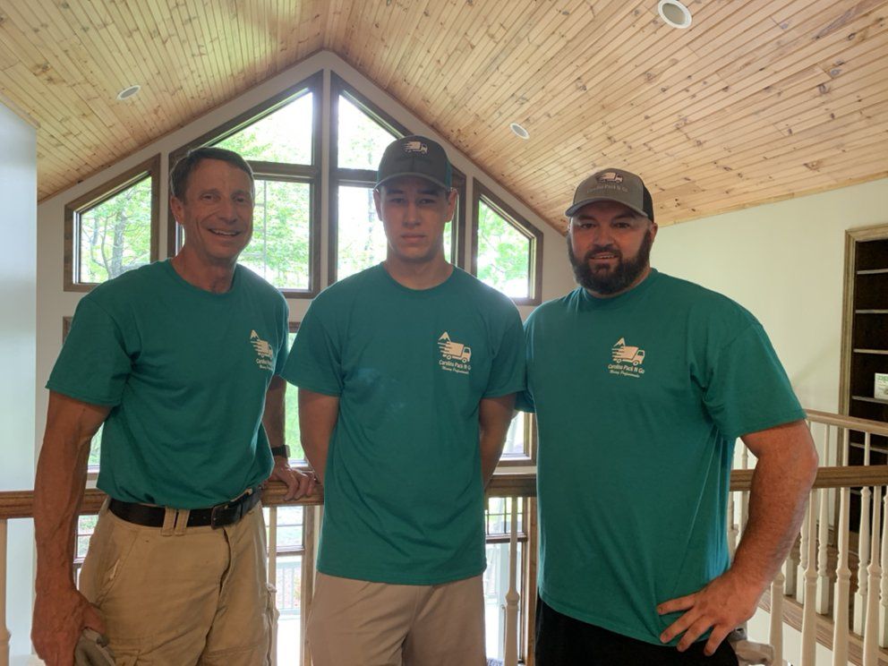 Three men in teal shirts stand in an open house, facing the camera.