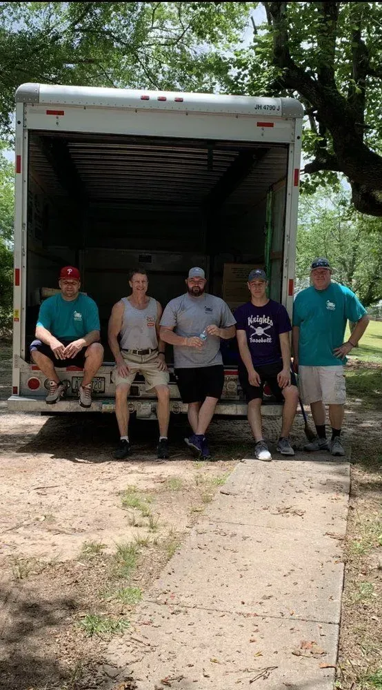 Five people stand in front of a moving truck. They are smiling, posed outside, ready for a move.