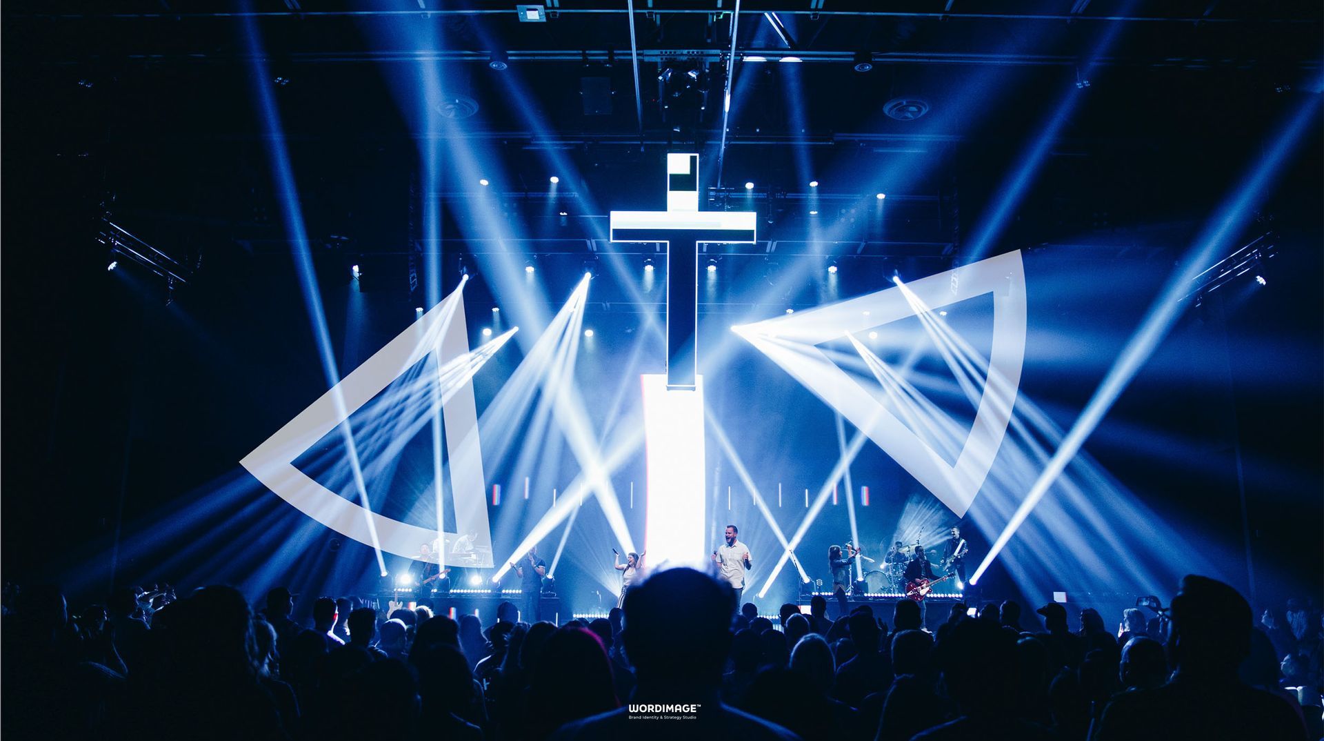 A group of people are sitting in front of a stage with a cross on it.