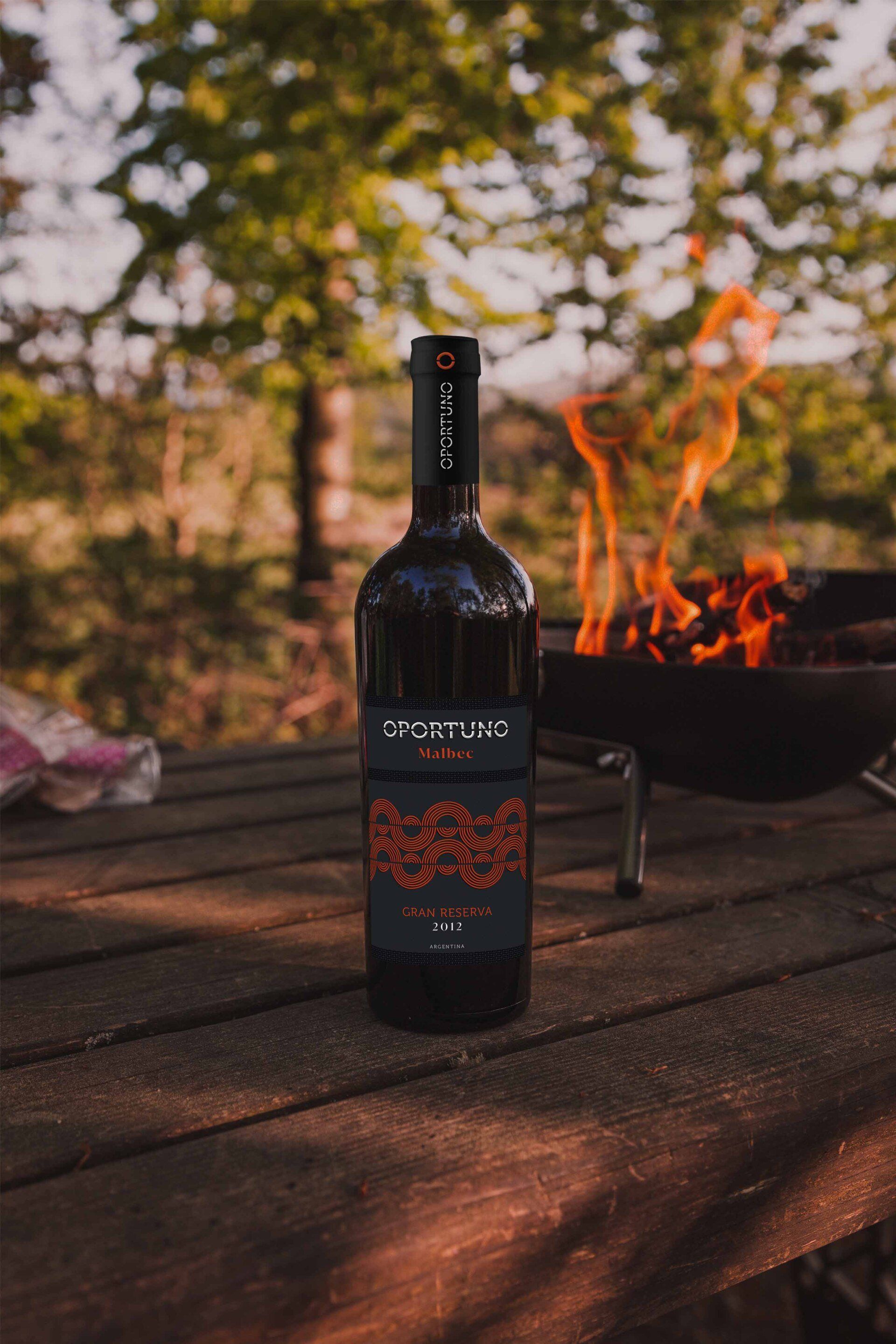 A bottle of wine is sitting on a wooden table next to a fire pit.