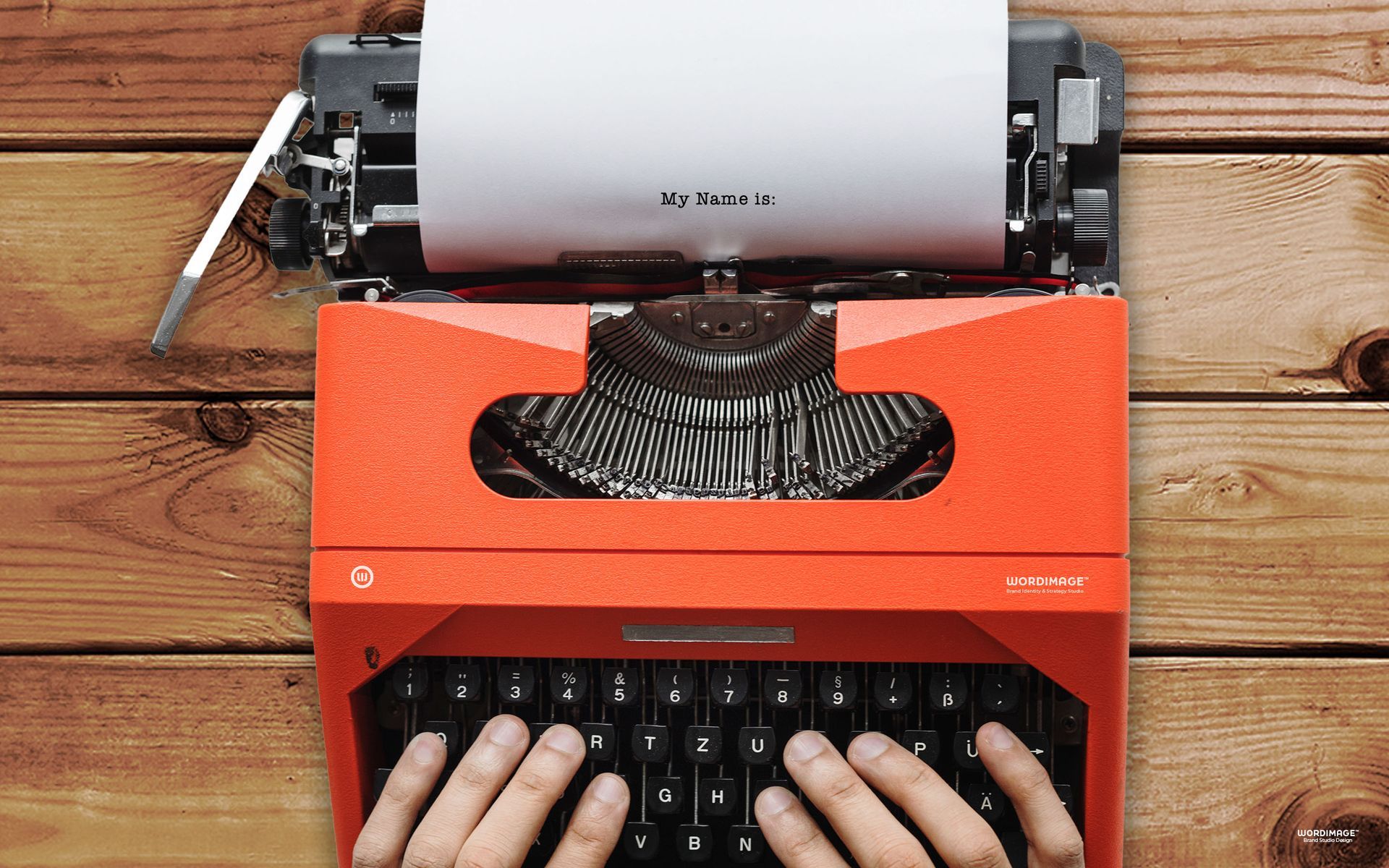 A person is typing on a red typewriter on a wooden table.