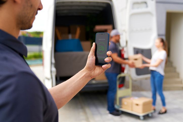 Un uomo tiene in mano un cellulare davanti a un furgone delle consegne.