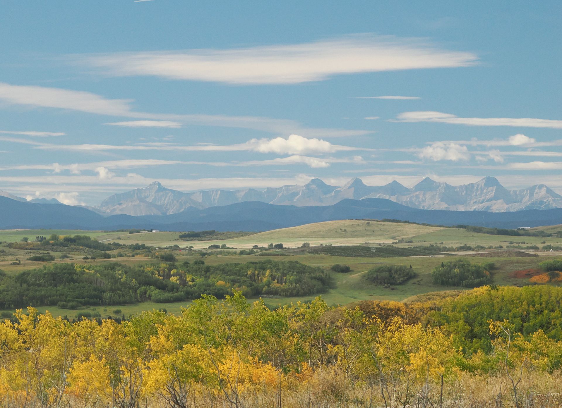 Rolling green hills with autumn foliage, distant mountains under a blue sky with clouds.