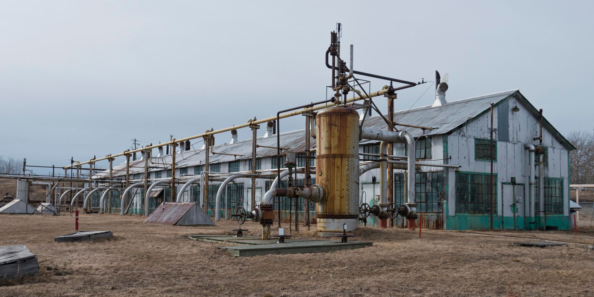 Old industrial building with pipes and weathered metal exterior against a cloudy sky.