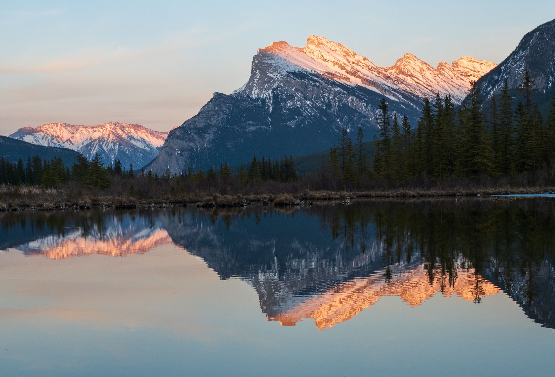 Snow-capped mountain range reflected in calm water at dawn; golden light.