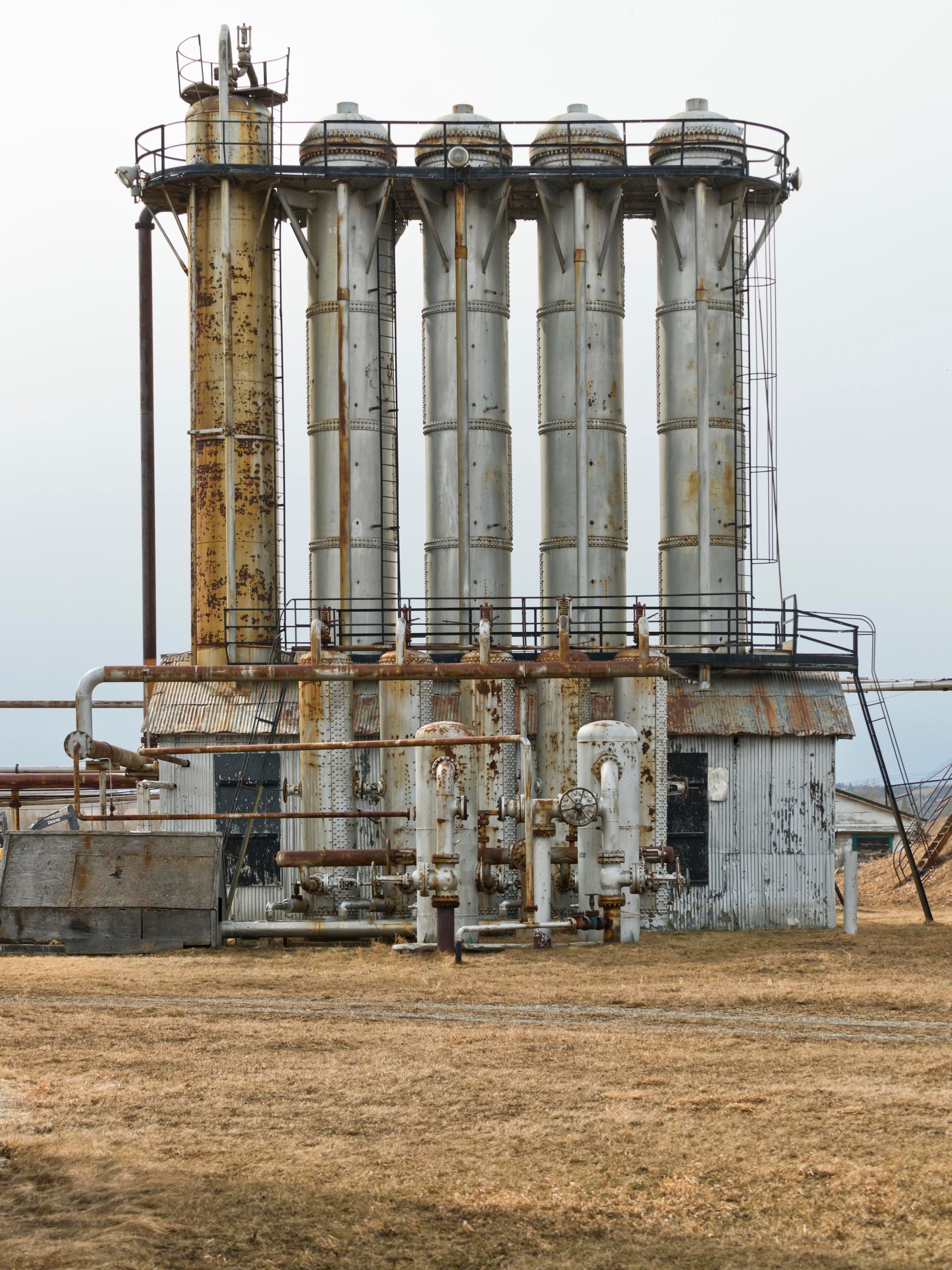 Rusty industrial processing plant with multiple vertical columns in a field.